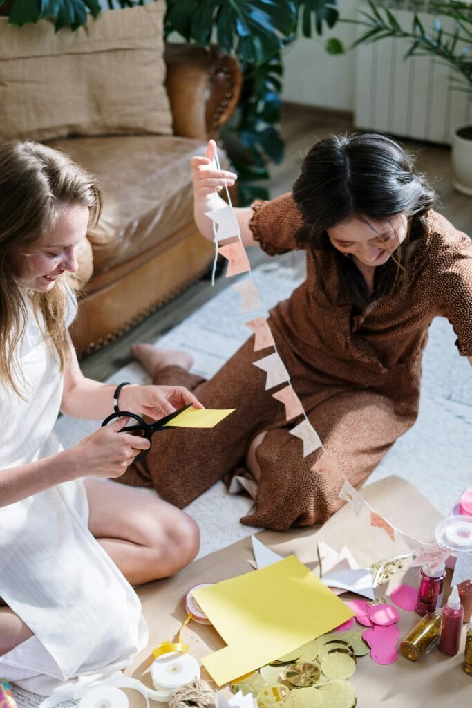 Two women enjoy crafting a paper garland together, smiling and relaxed indoors.