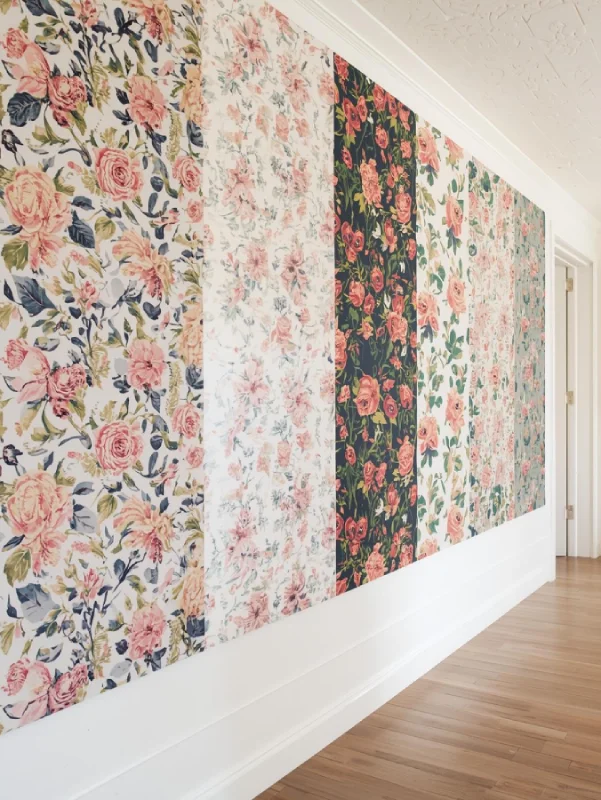 A creative studio or hallway with a gallery of different floral wallpaper panels in various global-inspired styles—vintage English, Moroccan florals, and tropical botanical prints. Eclectic and vibrant.