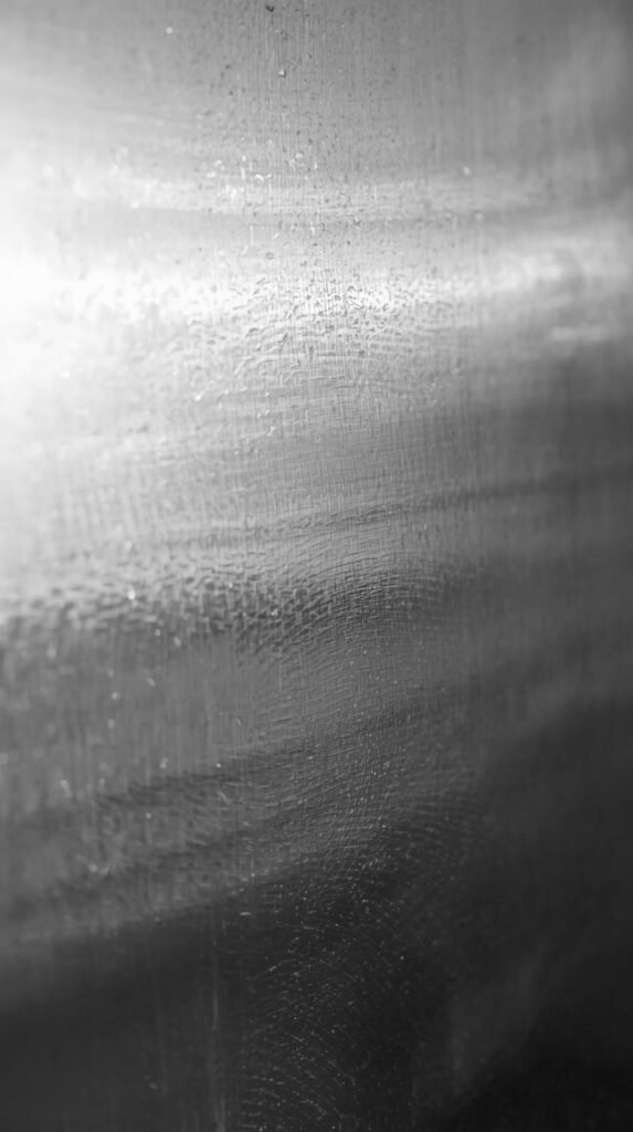 A close-up shot of a stainless steel refrigerator door showing subtle fingerprints and smudges. 