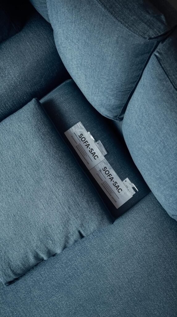 Fabric couch with the seat cushion lifted to reveal manufacturer cleaning tags underneath, soft textured blue upholstery.
