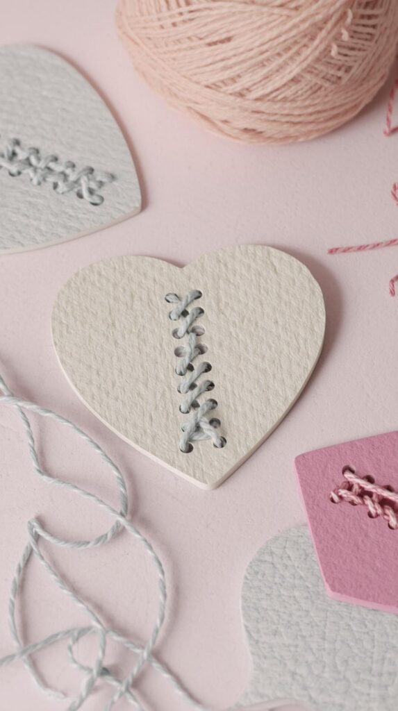 Heart-shaped lacing cards made from cardstock with colorful yarn threaded through holes, calm and focused craft scene, soft pastel tones.