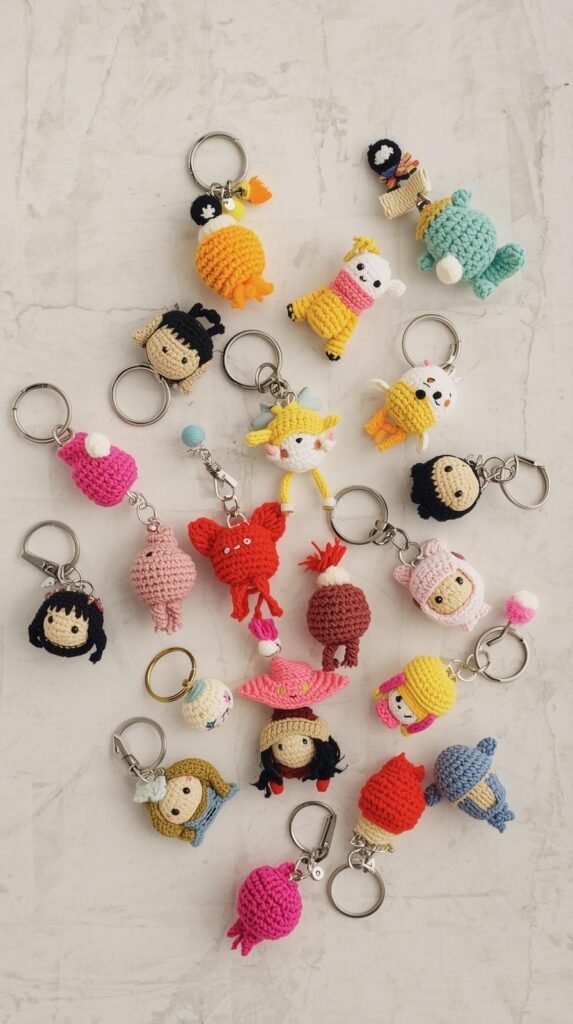 Crochet keychain charms laid out on a neutral background, small colorful yarn accents, metal key rings visible, playful handmade aesthetic