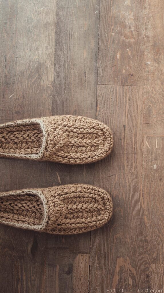 Crochet slippers placed side by side on a wooden floor, chunky yarn texture, cozy neutral tones, warm indoor lighting